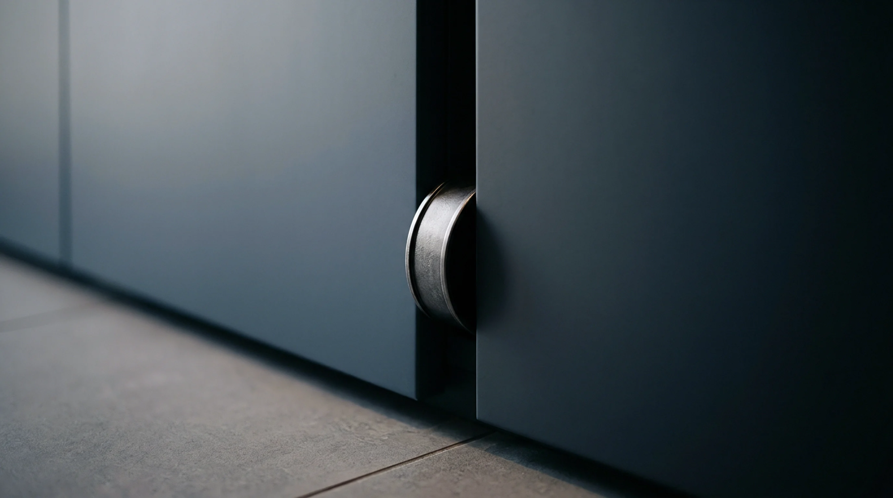 A cylindrical metal container stands wedged in the vertical gap between two dark grey matte partition panels above a grey tiled floor.